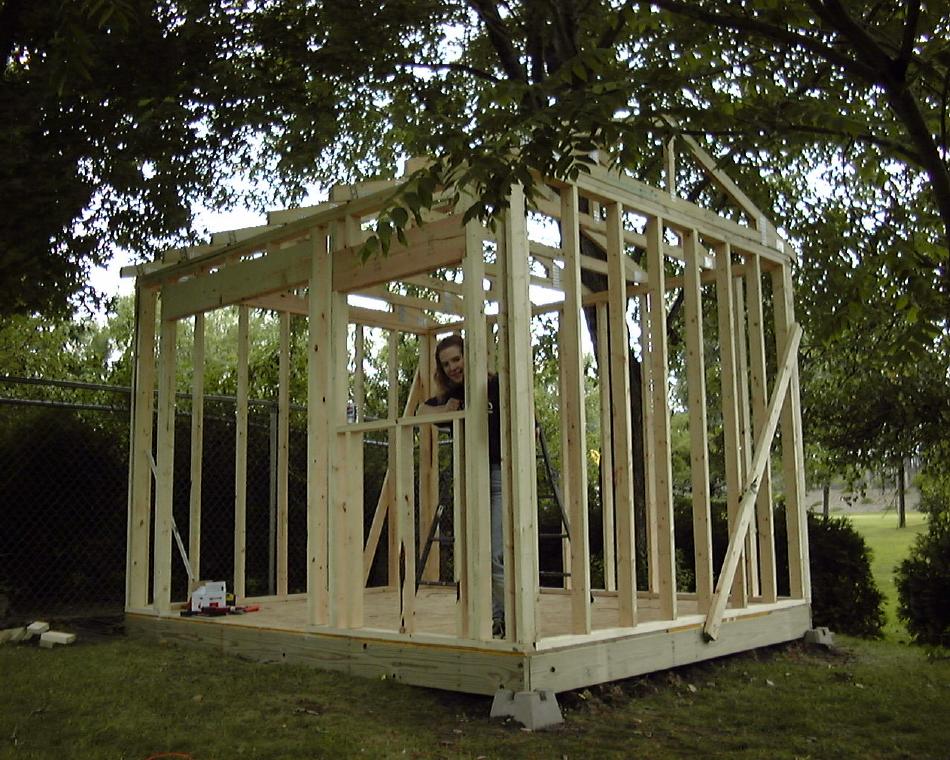 Framing Finished
We didn't pause to take any other photos-- this one shows where we stopped for the day when rain started falling.  The front of the building will have a roll-up door and a window (being demonstrated by Cathy).  We made good progress before the rain-- getting all the walls framed and trusses up and temporarily braced.

