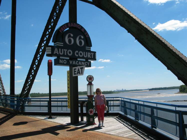 Route 66 Memorbelia
Partway across the bridge was an information area, with some nostalgic signs, an old gas pump, and an old car.  In this picture, Cathy poses near some of these.
